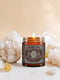 A high-quality studio photograph of the Grimoire & Goblet White Sage & Lavender candle. The 9 oz or 4 oz amber-colored glass jar is cylindrical with a smooth, black metal lid. The ornate, detailed label features the brand's name, 'Sage & Spirit,' an all-seeing eye, and the scent notes 'White Sage + Lavender.' The 100% soy wax blend and cotton wick are visible, crafted for a long-burning, clean, and elegant home fragrance. This piece of gothic home decor is a spiritual tool for energy cleansing.